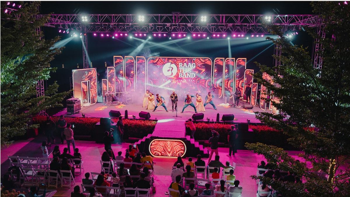 An open-air stage lit in pink with an audience seated in front